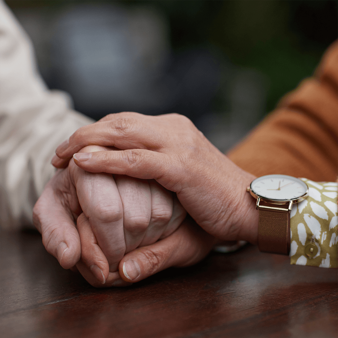 a women's hands are loving over a man's hands in comfort as they both sit at the kitchen table to decide how to handle his Alzheimer's diagnoses 